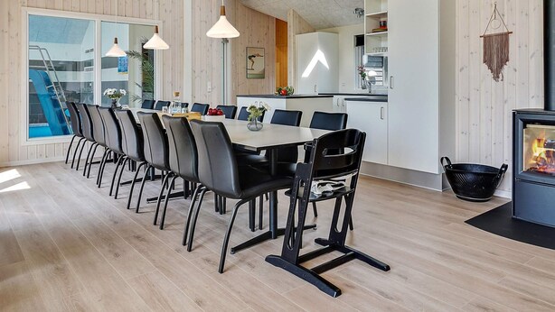 A modern dining area with a long table and chairs, a kitchen area with a stove, and a view of a swimming pool. - Chic Holiday Home in Hovedstaden near Sea (Vejby)