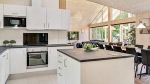 A modern kitchen with white cabinetry, a central island, and a dining area with a view of the outdoors. - Chic Holiday Home in Hovedstaden near Sea (Vejby)