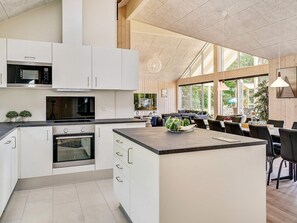 A modern kitchen with white cabinetry, a central island, and a dining area with a view of the outdoors. - Chic Holiday Home in Hovedstaden near Sea (Vejby)