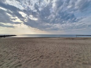 Una playa con un promontorio rocoso en la distancia, una orilla arenosa y un cielo nublado.