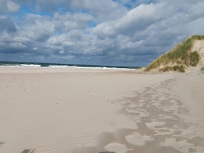 A beach with sand, waves, and a grassy dune.