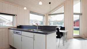 A modern kitchen with a central island, a dining area with a table and chairs, and large windows providing natural light. - Holiday Home in Großenbrode (Grossenbrode)