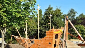 A wooden pirate ship play structure with climbing nets and slides, surrounded by trees. - Holiday Home in Großenbrode (Grossenbrode)