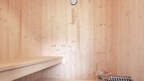 Un cuarto de sauna con paredes y banco de madera, un termómetro en la pared y una piedra para lavarse.