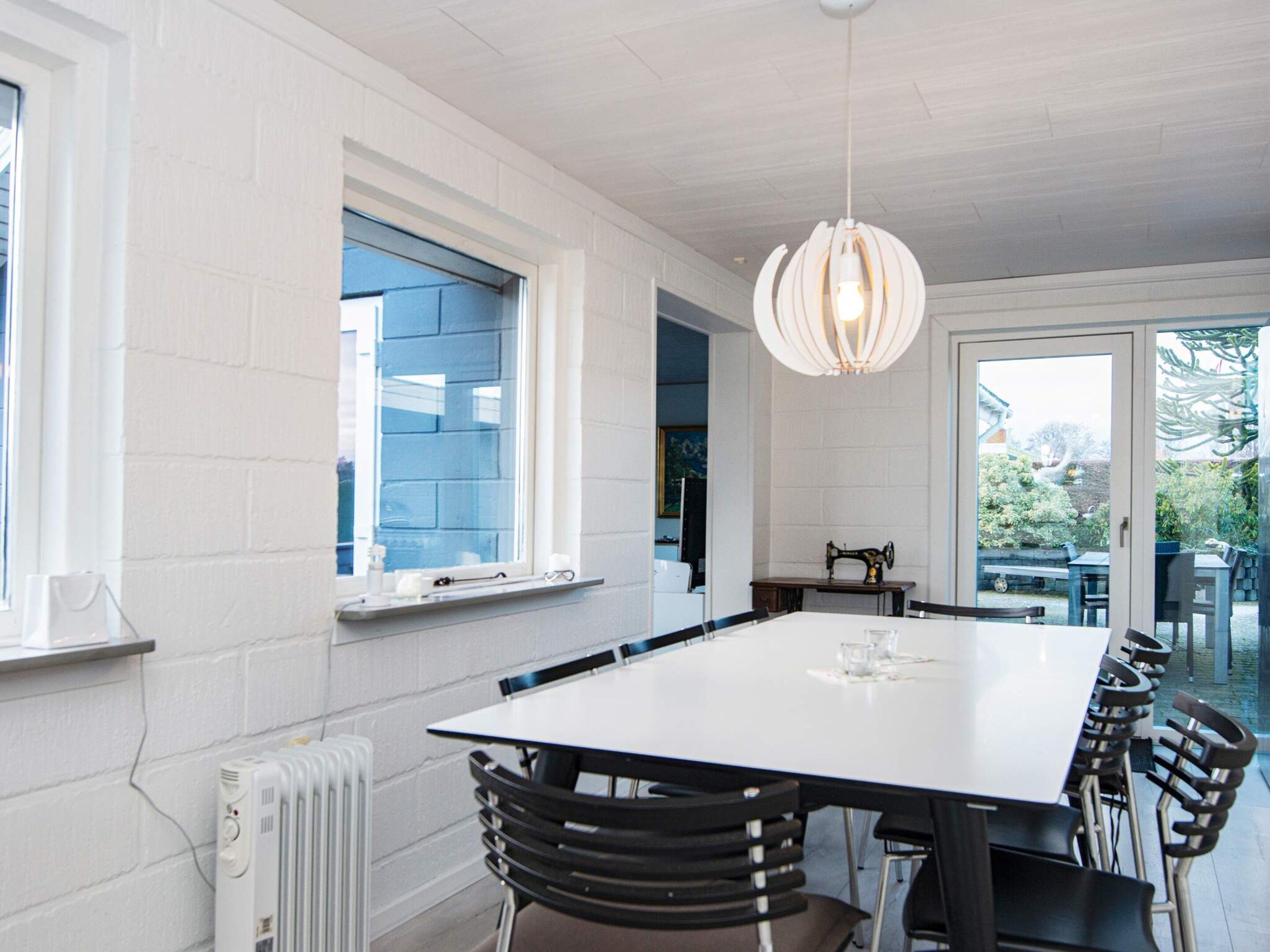 A dining area with a white table and chairs, a radiator, a window with blue shutters, and a hanging light fixture.