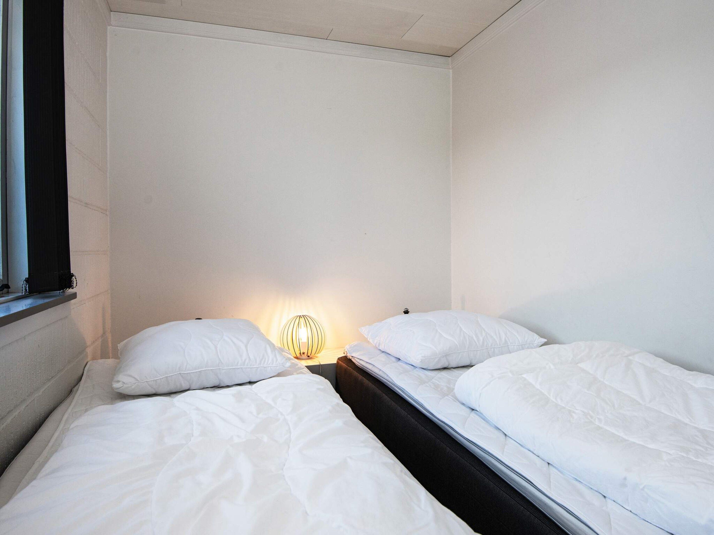 A single bed with white bedding in a room with plain walls and a window.