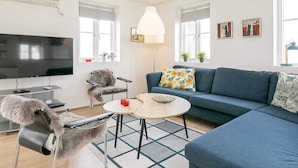 Una sala de estar moderna con una televisión de pantalla plana, un sofá, un sillón, una mesa de centro y una lámpara.