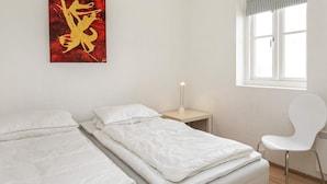 Un dormitorio con dos camas, una mesita de noche con lámpara, una silla y una ventana con vistas.