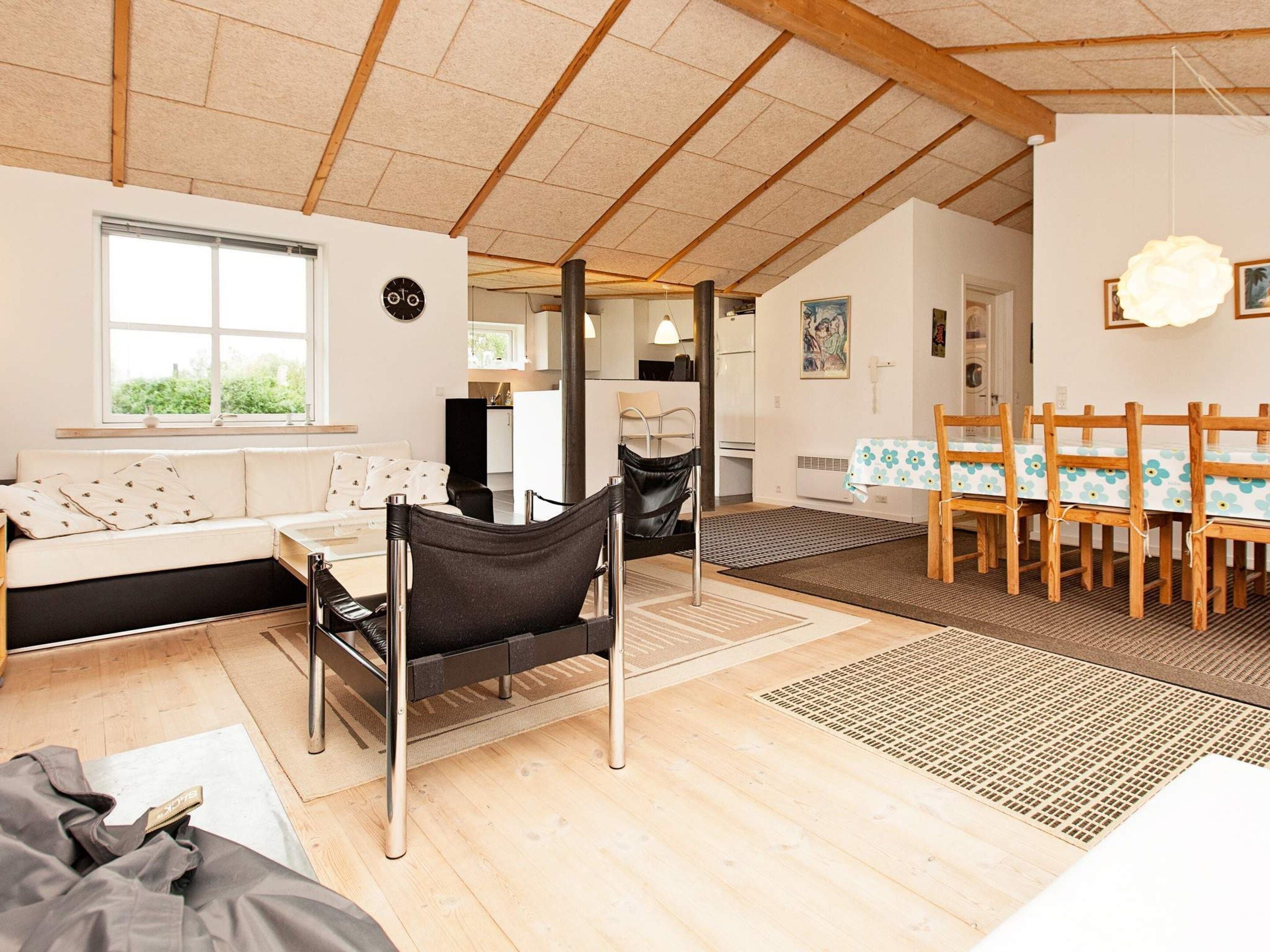A spacious living area with a sofa, a dining table with chairs, a black chair, and a wooden ceiling.