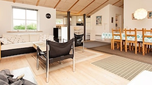 A spacious living area with a sofa, a dining table with chairs, a black chair, and a wooden ceiling.