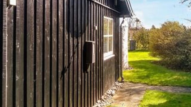 A wooden building with a window and a door, a stone pathway, and a grassy area.