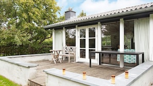 A covered outdoor area with a table and chairs, a stone wall, and a wooden deck.