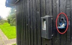A black metal gate with a rectangular lockbox and a circular security camera.