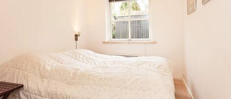 A bedroom with a bed, a window, a wall-mounted light, and a wooden floor.