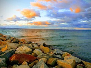 A rocky shoreline with a person surfing in the distance, under a colorful sky. - 6 Person Holiday Home in Dronningmolle-by Traum (Dronningmolle)