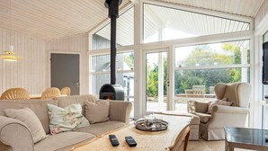 Ein gemütliches Wohnzimmer mit einer Couch, einem Couchtisch und einem Kamin. Im Hintergrund stehen Stühle und ein Fernseher.