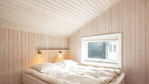 Ein Schlafzimmer mit holzverkleideter Schräge, einem Einzelbett mit weißer Bettwäsche, zwei Wandleuchten und einem Fenster mit Jalousien.