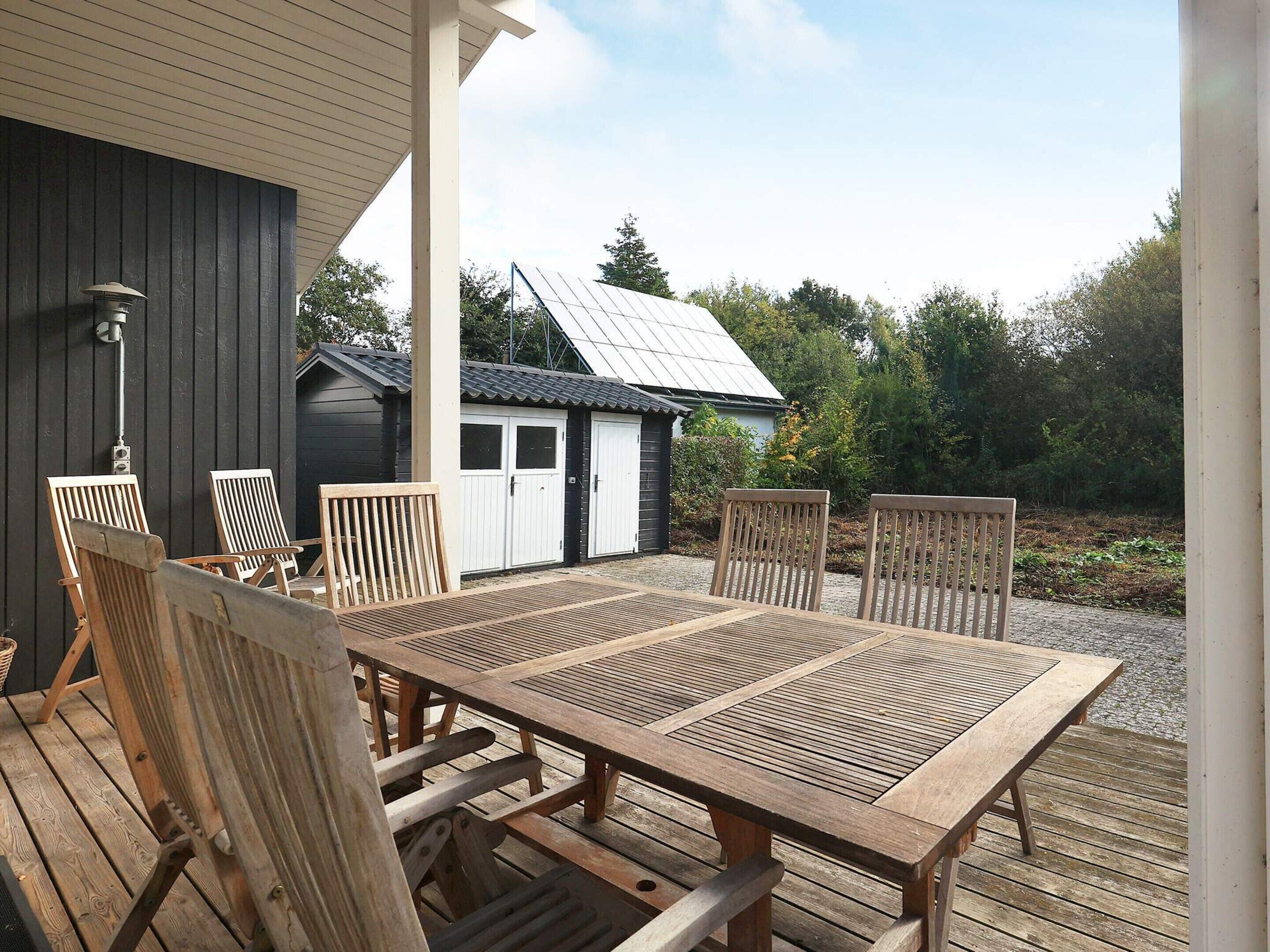An outdoor wooden deck with a table and chairs, a small shed, and a solar panel in the background.