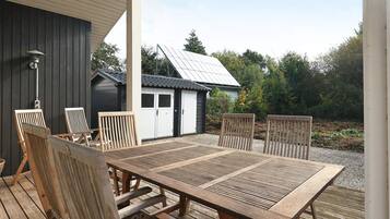 An outdoor wooden deck with a table and chairs, a small shed, and a solar panel in the background.