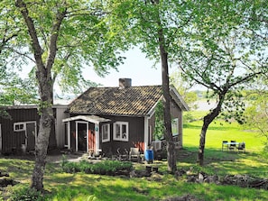 Una casa rústica con techo inclinado, un porche delantero y un pequeño jardín con una mesa y sillas.