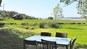 Una mesa y cuatro sillas en un entorno al aire libre, con un campo de césped, un muro de piedra y un edificio de madera al fondo.