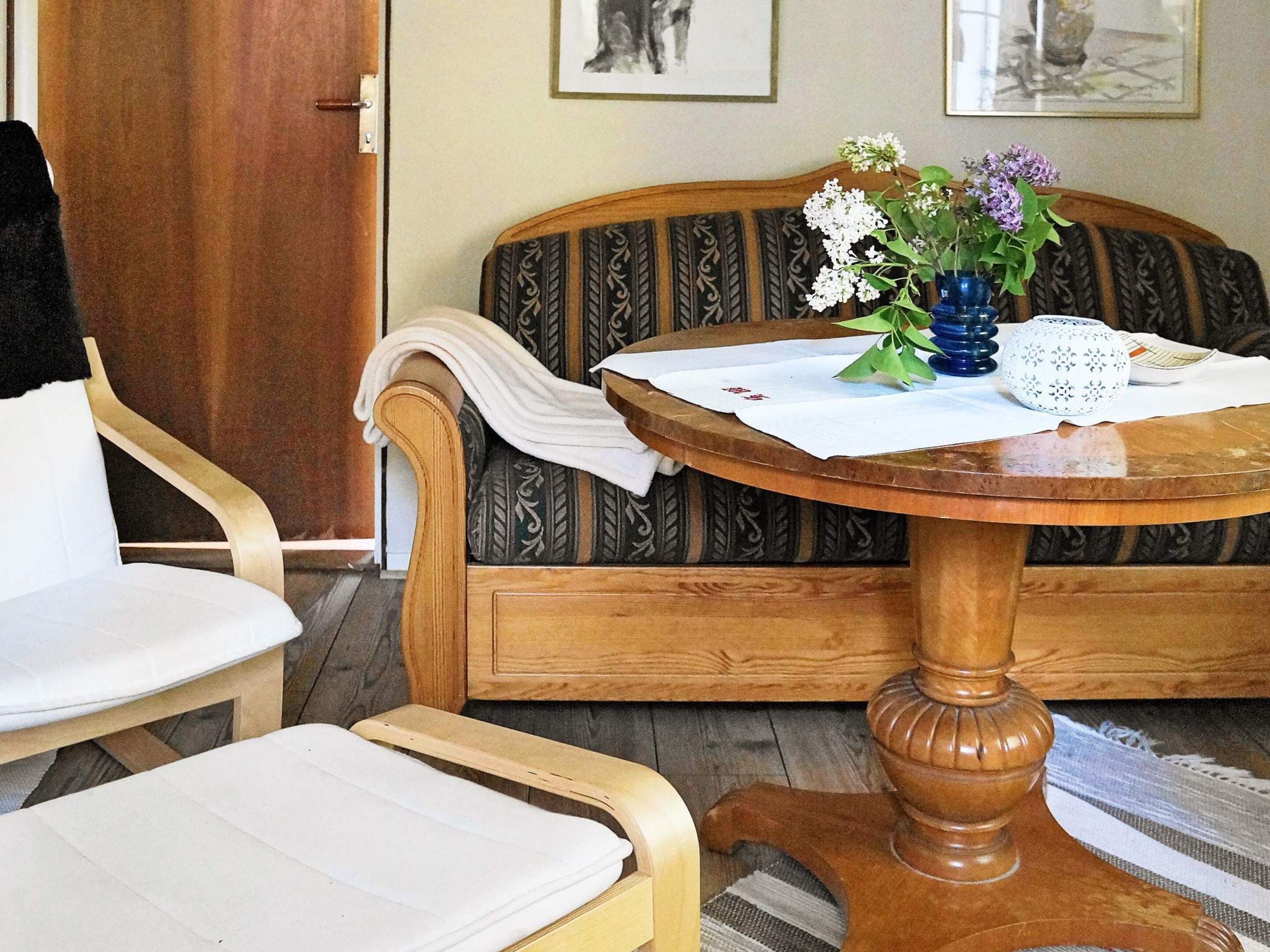 A room with a wooden sofa, a round wooden table with a white cloth, and a chair.