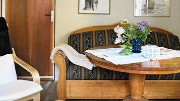 A room with a wooden sofa, a round wooden table with a white cloth, and a chair.