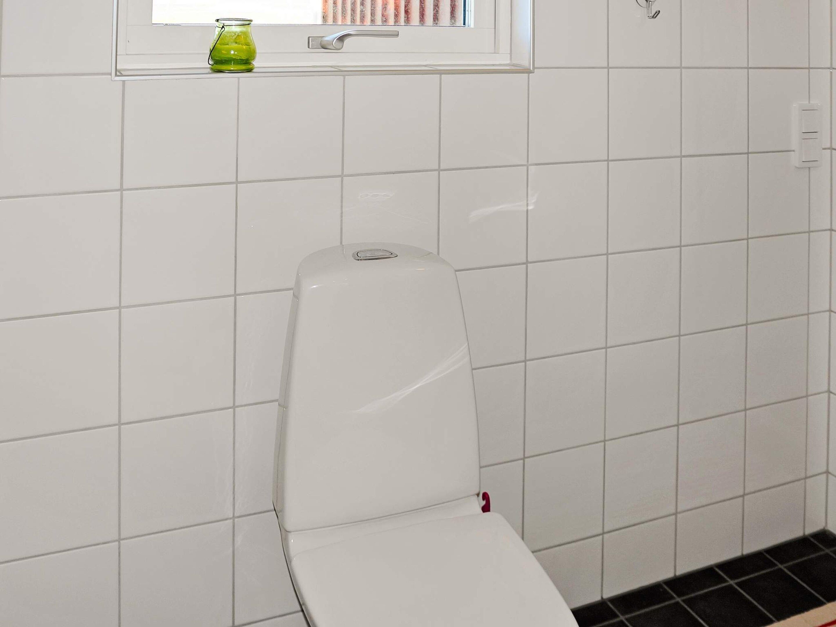 A white toilet in a bathroom with white tiled walls and a window above it.