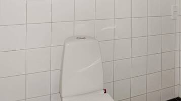 A white toilet in a bathroom with white tiled walls and a window above it.