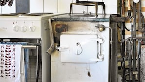 Una cocina vintage con estufa, un electrodoméstico blanco grande y tuberías a la vista.
