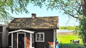 A rustic house with a tiled roof, a small porch, and a garden with outdoor furniture.