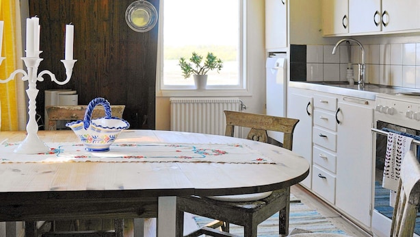 Una cocina con una mesa redonda, sillas, estufa, armarios y una ventana con una planta.
