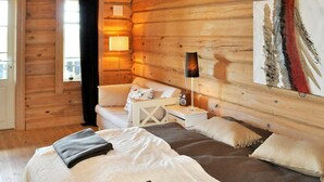 A cozy log cabin bedroom with a bed, a nightstand, a lamp, and a painting on the wall.