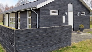 A dark wooden cottage with a small porch, a white door, and a window with shutters. - 8 Person Holiday Home in Hals-by Traum (Hals)
