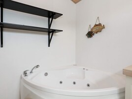 Un baño con una bañera blanca, repisas metálicas negras y un adorno de pez en la pared.