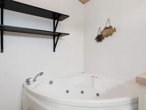 Ein Badezimmer mit einer weißen Badewanne, schwarzen Metallregalen und einer Wanddekoration mit einem Fisch.
