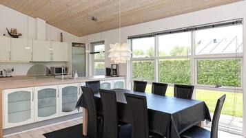 A modern kitchen with a dining area, large windows, and a view of greenery.