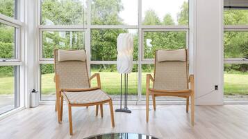A room with large windows, two wooden chairs with cushions, and a glass table.