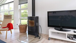 Una sala moderna con chimenea, un televisor sobre un mueble bajo, una cesta de mimbre y un sillón con una manta roja.