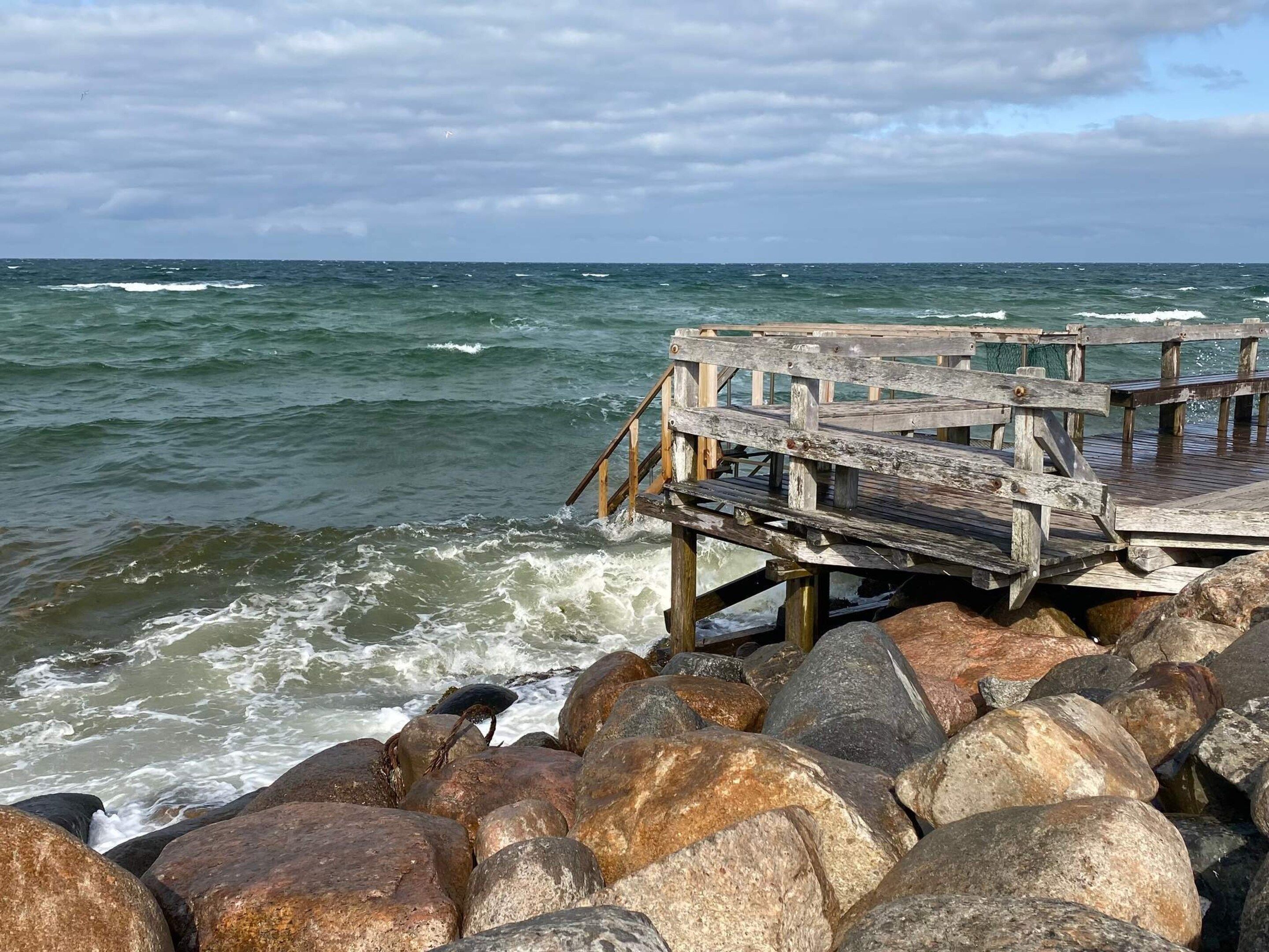 A wooden pier extending over a rocky shoreline with waves crashing against it.