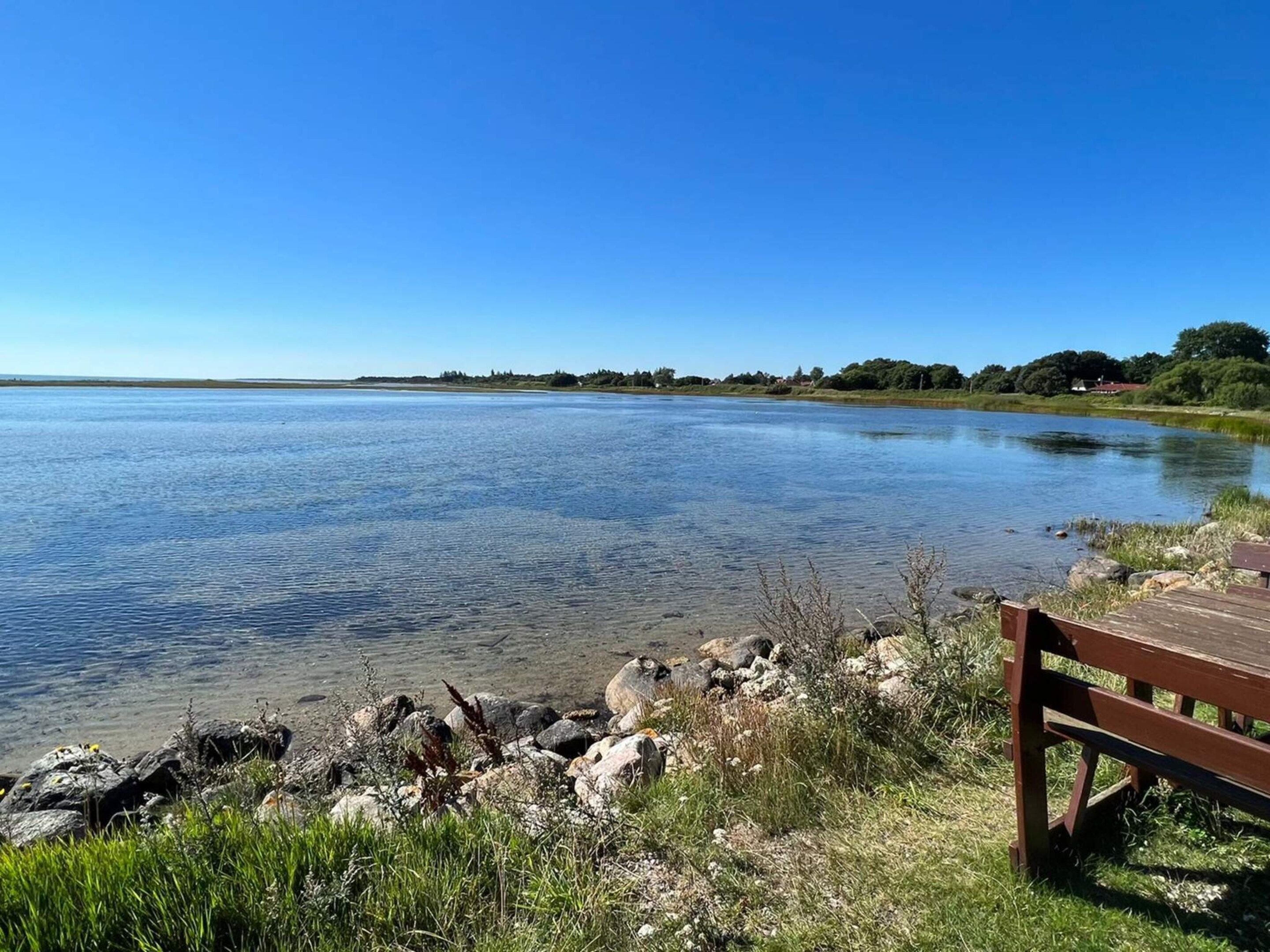 Un lago tranquillo con una panchina di legno sulla riva, circondato da rocce ed erba.
