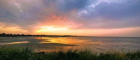 A coastal landscape with a sunset, grassy foreground, and distant shoreline.