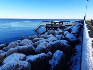 A pier with a metal railing, large rocks, and a clear blue sky.