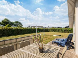 An outdoor patio area with a wooden table, chairs, a potted plant, and a swing set in the background. - Pleasing Holiday Home in Haderslev near Sea (Haderslev)