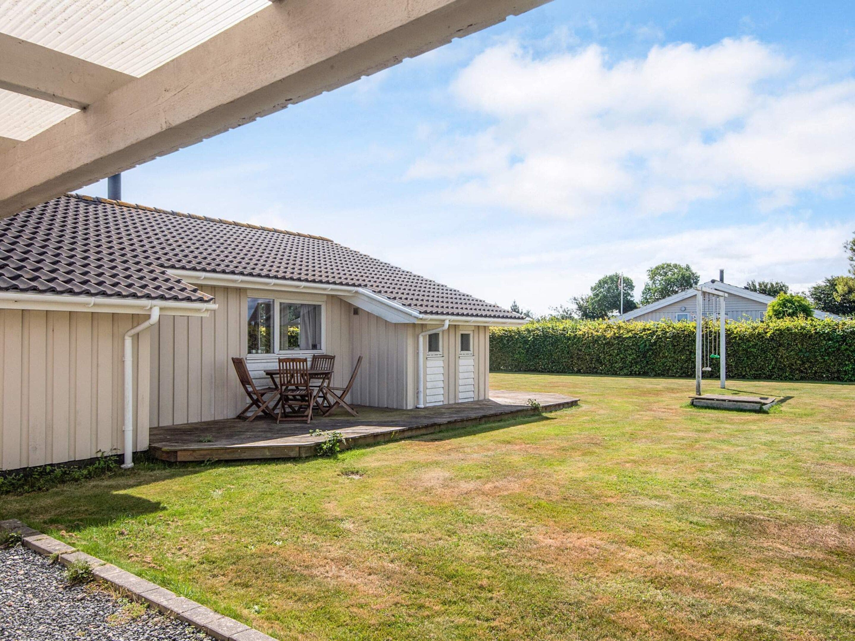 A single-story house with a tiled roof, a small porch with a table and chairs, and a well-maintained lawn.