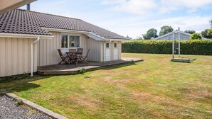 A single-story house with a tiled roof, a small porch with a table and chairs, and a well-maintained lawn. - Pleasing Holiday Home in Haderslev near Sea (Haderslev)