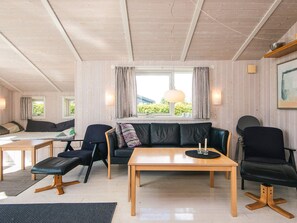 A cozy living room with a wooden ceiling, a black leather sofa, a wooden coffee table, and a small dining table with chairs. - Pleasing Holiday Home in Haderslev near Sea (Haderslev)