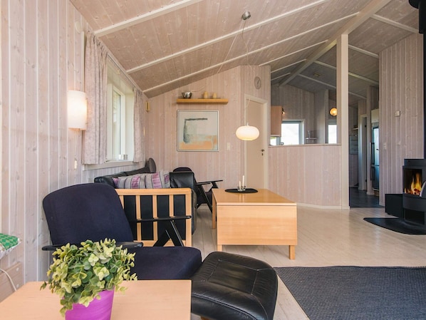 A cozy living room with a wooden ceiling, a dining area with a table and chairs, a fireplace, and a large window. - Pleasing Holiday Home in Haderslev near Sea (Haderslev)