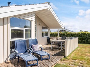 A covered outdoor deck with lounge chairs and a table, adjacent to a house with large windows and a white exterior.