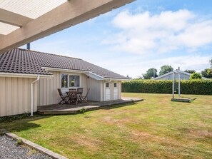 A single-story house with a tiled roof, a covered patio with a table and chairs, and a well-maintained lawn.